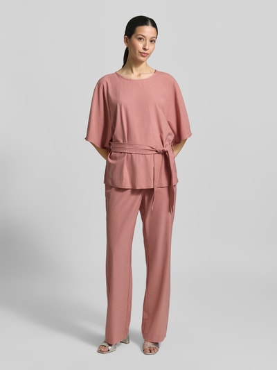 Frauenmodel trägt Hose aus Viskose-Mix Modell 'Bai Roy' von MOS MOSH in Rosa, schmal geschnitten, mit elastischem Bund und Gesäßtaschen, Ganzkörperansicht von vorne.