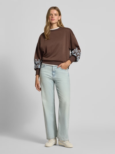 Frauenmodel trägt Relaxed Fit Sweatshirt aus reiner Baumwoll-Mix Modell 'BROOKE' von ONLY, braun mit Blumenmuster, Damen Sweatshirt, Ganzkörperansicht von vorne.