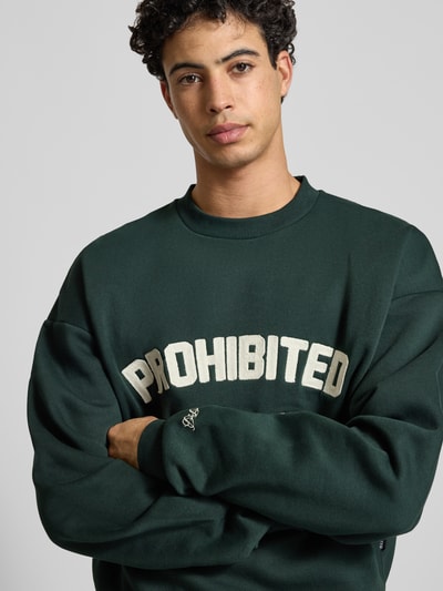 Männermodel trägt Oversized Sweatshirt mit Label-Detail von PROHIBITED, dunkles Grün, Baumwoll-Mix, Rundhalsausschnitt, Nahaufnahme Oberkörper.