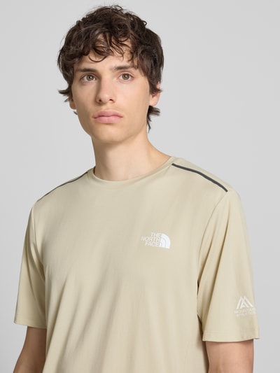 Männermodel trägt T-Shirt mit Logo und Rundhalsausschnitt von The North Face in regular fit, lichtbeige, model 'MOUNTAIN ATHLETICS', korte mouwen, close-up bovenlichaam vooraan.