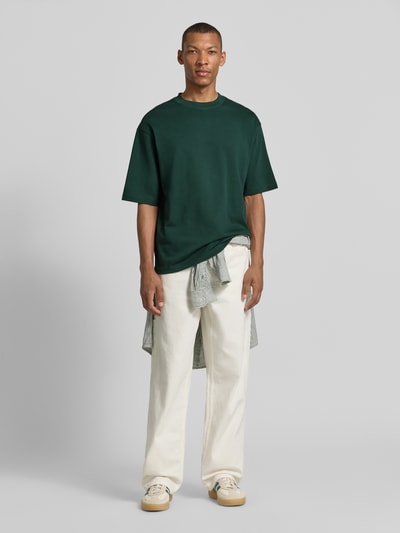 Męski model trägt Regular Fit T-Shirt aus reiner Baumwolle Modell 'HASPEN' von SELECTED HOMME, ciemnozielony kolor, gładka tekstura, Ganzkörperansicht von vorne.