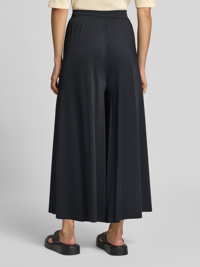 Männermodel trägt Wide Leg Hose mit Tunnelzug von Oui, czarne spodnie z szerokimi nogawkami, Mieszanka materiałów z dodatkiem streczu, elastyczny pas, tunel, Szerokość w rozmiarze 36: 37 cm, Długość wewnętrzna nogawki w rozmiarze 36: 61 cm, Ganzkörperansicht Rückansicht