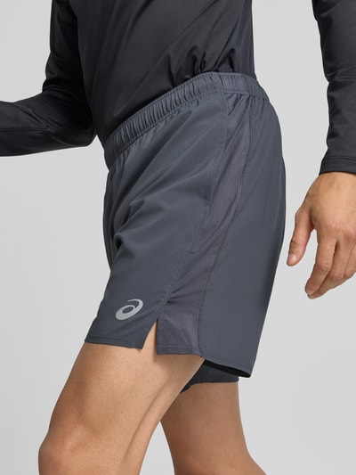 Männermodel trägt Shorts mit elastischem Bund und Logo von ASICS in Dunkelgrau, glatte Textur, Nahaufnahme Oberschenkel, Regular Fit, Innenhose, Bundweite 37 cm, Innenbeinlänge 45 cm