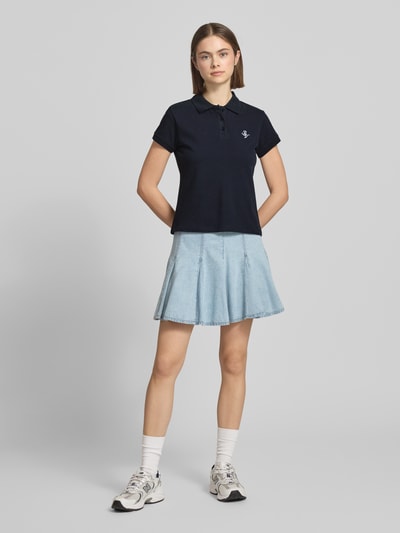 Vrouwenmodel draagt kortärmliges poloshirt in piquéoptik mit kragen und logostickerei van REVIEW, puur katoen, slim fit, polokraag, geborduurd logo, ruglengte maat S 52 cm, effen donkerblauw, lichte denim rok, ganzebodyshot van voren.