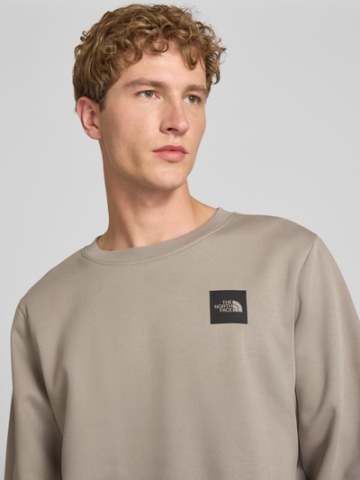 Männermodel trägt Regular Fit Sweatshirt mit Logo-Detail van The North Face in beige katoenmix, logodetail op de borst, Nahaufnahme Oberkörper. Ruglengte maat M: 60 cm, mouwlengte maat M: 70 cm.