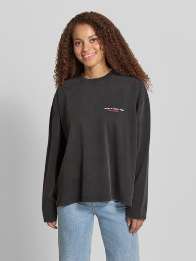 Frauenmodel trägt Oversized Longsleeve mit Logo-Print Modell 'Memories' von Karo Kauer, Reine Baumwolle, Oversized-Fit, Rundhalsausschnitt, überschnittene Schultern, Rückenlänge bei Größe S: 63 cm, dezentes Schwarz mit weicher Textur, glänzender Print, Ganzkörperansicht von vorne.