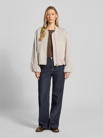 Modelka nosi Regular Fit Blouson mit Baseball-Kragen od Marc O'Polo, efekt: jednolity kolor, bufiaste rękawy, długi rękaw, wpuszczane kieszenie, krój regular fit, zamek błyskawiczny, materiał z recyklingu, jasna kolorystyka, gładka faktura, widok całej sylwetki z przodu.