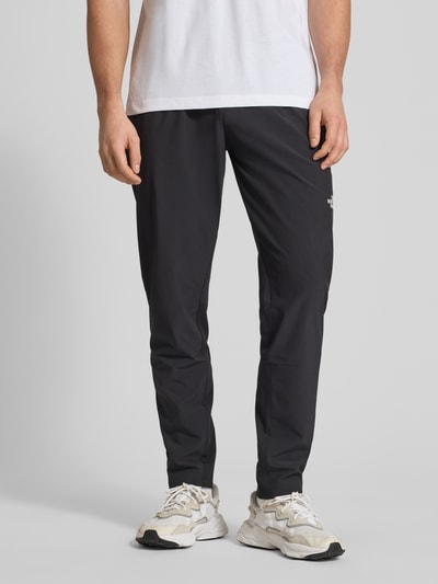 Männermodel trägt schwarze Trainingshose mit elastischem Bund und Logo von The North Face aus Material-Mix mit Stretch-Anteil, Regular-Fit, Ganzkörperansicht von vorne.