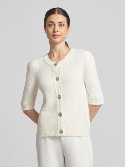 Modelka kobieca nosi Cardigan in Strick-Optik Modell 'Marle' od GUIDO MARIA KRETSCHMER WOMAN, biała faktura dzianiny, krój slim fit, okrągły dekolt, zapięcie na guziki z kryształkami, rękaw 3/4, żebrowane wykończenia, długość pleców w rozmiarze 36: 57 cm, widok całej sylwetki od przodu.