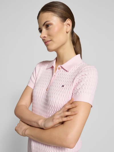 Frauenmodel trägt Slim Fit Poloshirt aus reiner Baumwolle von Tommy Hilfiger in Rosa mit Zopfmuster, Polokragen und Logo-Detail, Nahaufnahme Oberkörper.