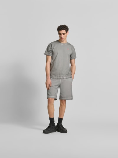 Männermodel trägt Sweatshorts aus reiner Baumwolle von Diesel in Grau, lockere Passform, elastischer Bund, Used-Look, Label-Print, Ganzkörperansicht von vorne.