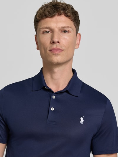Männermodel trägt Regular Fit Poloshirt aus Baumwoll-Mix Modell 'TOUR PIQUE' von Polo Ralph Lauren in Dunkelblau, Logo-Detail, Nahaufnahme Oberkörper.