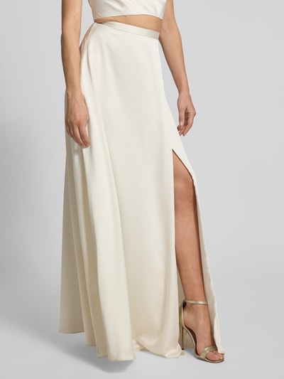 Frauenmodel trägt Relaxed Fit Abendkleid mit Gehschlitz von Jake*s Cocktail in cremefarbener Satin-Optik, Detailaufnahme, Gehschlitz sichtbar.