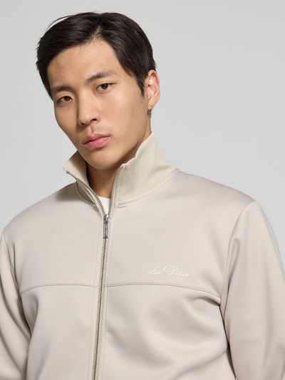 Mężczyzna nosi Sweatjacke mit Logo-Print Modell 'Ballier' od Les Deux, beż, gładka faktura, stójka, zamek, zbliżenie na górną część ciała
