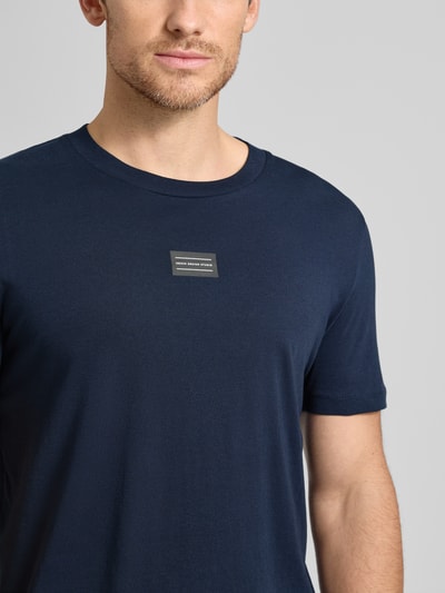 Männermodel trägt Regular Fit T-Shirt aus reiner Baumwolle von Tom Tailor Denim in Dunkelblau mit Label-Schriftzug, Nahaufnahme Oberkörper.