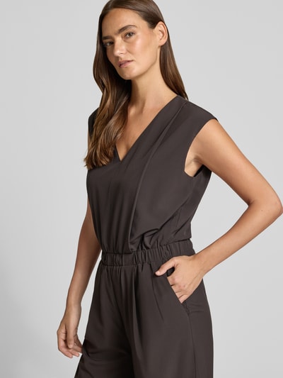 Kobiece modelka nosi kombinezon Relaxed Fit Jumpsuit mit V-Ausschnitt model 'Charlou' od Someday, elastyczna mieszanka materiałów, ciemny kolor, wpuszczane kieszenie, taliowany krój, bez rękawów, dekolt w serek, wpuszczane kieszenie, całkowita długość 146 cm w rozmiarze 36, szerokość w rozmiarze 36: 52 cm, długość tyłu w rozmiarze 36: 44 cm, długość wewnętrzna nogawki w rozmiarze 36: 71 cm, zbliżenie na górną część ciała
