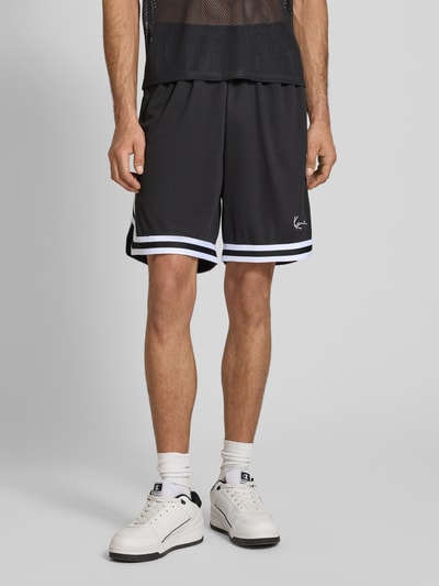 Männermodel trägt Relaxed Fit Shorts mit Logo-Stitching von KARL KANI in Schwarz, Mesh, elastischer Bund, Ganzkörperansicht von vorne.