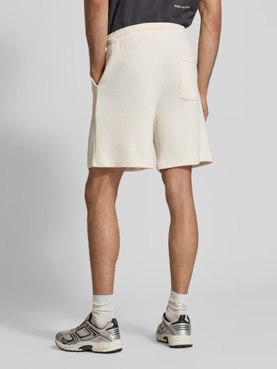 Männermodel trägt Shorts aus Baumwoll-Mix mit Strukturmuster Modell 'KNOX' von Redefined Rebel in Creme mit elastischem Bund und Tunnelzug, Ganzkörperansicht Rückansicht.