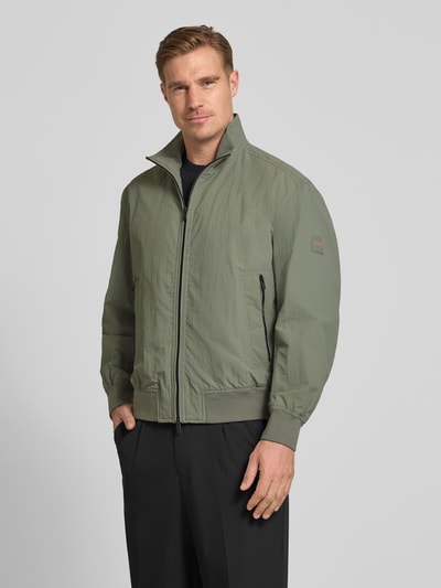 Männermodel trägt Relaxed Fit blouson aus waterafstotend materiaal model 'OPENS' van BOSS Orange, look: effen, opstaande kraag, tweewegritssluiting, labelpatch, lange mouw, mouwboord en rompzoom geribd, zij-steekzakken, ganzkörperansicht van voren.