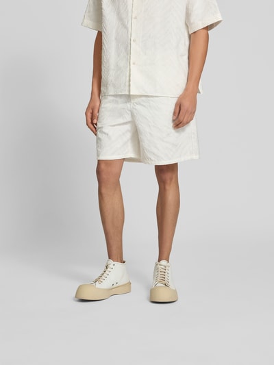 Męski model nosi Shorts mit Strukturmuster od Kenzo z czystej bawełny, krój straight fit, jasny kolor, widoczne kieszenie i zapięcia, szerokość w rozmiarze M 44 cm, długość nogawki 19 cm, widok całej sylwetki z przodu.