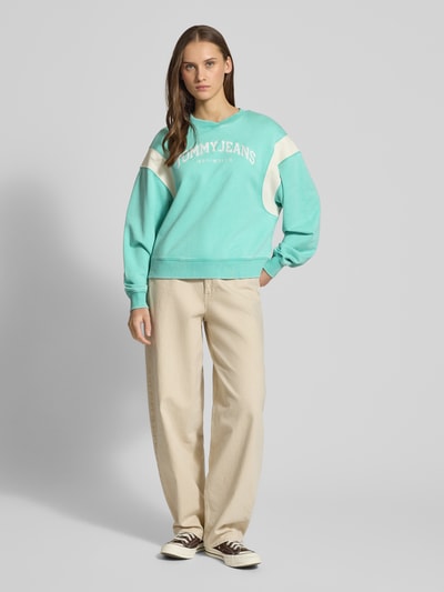 Vrouwenmodel draagt Boxy Fit Sweatshirt uit katoenmix model 'VARSITY CREW' van Tommy Jeans, two tone look, ribgebreide details, label stitching, lange mouwen, crew neck, sweatmateriaal, voorkant volledige lichaamsweergave.
