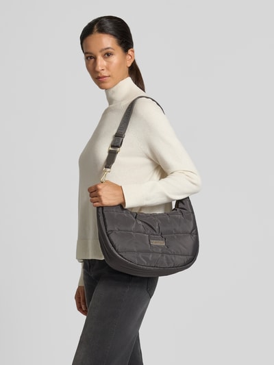 Vrouwenmodel draagt Shoulder-Bag in Stepp-Optik Modell 'Lifetime Buddy' van Hey Marly, grijs, rechthoekige vorm, gladde gewatteerde textuur, met logo en verstelbare, afneembare riem, hoofdvak met rits, breedte 36 cm, lengte 28 cm, diepte 11 cm, riem 110 cm, zijaanzicht, geheel lichaamsopname van voren.