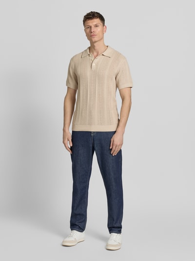 Männermodel trägt Slim Fit Poloshirt mit Knopfleiste von Jack & Jones Premium aus Baumwoll-Mix in Beige, Polokragen, Ganzkörperansicht von vorne.