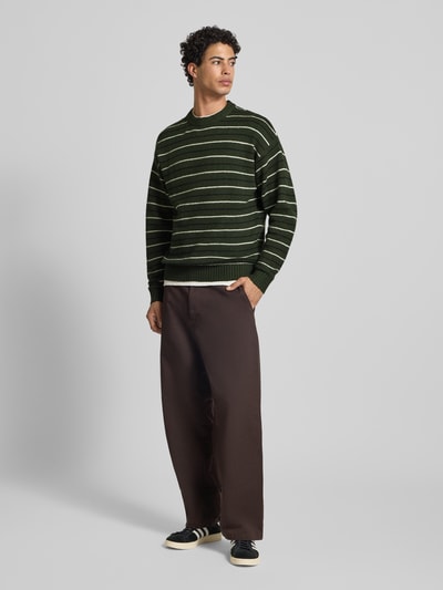 Mannelijk model draagt Strickpullover mit Streifenmuster Modell 'SOHO OLLIE' van Jack & Jones, relaxed fit, katoenmix, groen met witte strepen, ronde hals, volledige lichaamsvoorzijde.