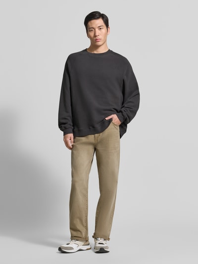 Männermodel trägt Sweatshirt mit Rundhalsausschnitt Modell 'ATUBAY' von American Vintage aus Baumwoll-Elasthan-Mix, Relaxed-Fit, schwarze Farbe, kombiniert mit heller Hose, Ganzkörperansicht von vorne, Rückenlänge bei Größe M/L: 67 cm, Ärmellänge: 77 cm.