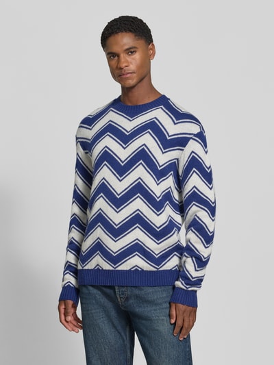 Männermodel trägt Strickpullover aus Schurwolle-Mix mit Rundhalsausschnitt von Armani Exchange, blau-weißes Zickzackmuster, Regular Fit, gerippte Abschlüsse, Rückenlänge 65 cm, Ärmellänge 69 cm, Ganzkörperansicht von vorne.