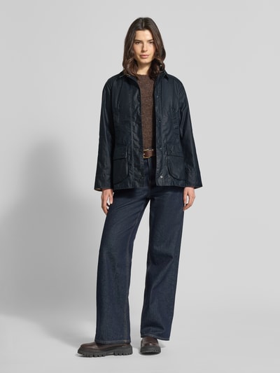 Modelka kobieca nosi Wachsjacke aus reiner Baumwolle von Barbour, ciemny granat, krój regular fit, teksturowana bawełna, przód z patkami, widok całej sylwetki z przodu.