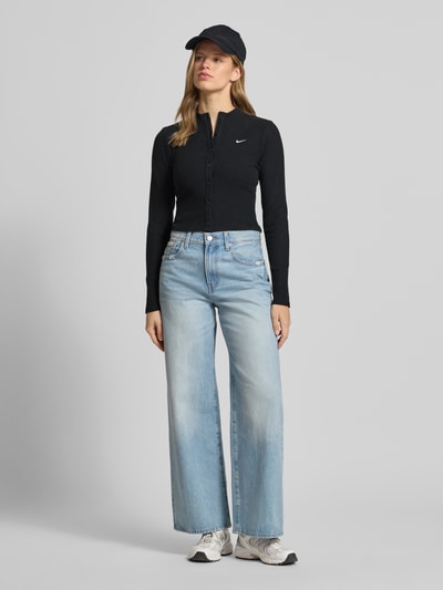 Frauenmodel trägt Cardigan in Ripp-Optik Modell 'CHILL' von Nike, Skinny-Fit, Stehkragen, Label-Stitching, langärmelig, durchgehende Knopfleiste, schwarze Farbe, strukturierte Oberfläche, Ganzkörperansicht von vorne.