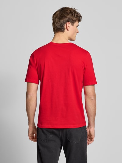 Mężczyzna model nosi czerwone T-Shirt z bawełny z nadrukiem label CORP od JACK & JONES, prosty krój, widok całej sylwetki z tyłu.