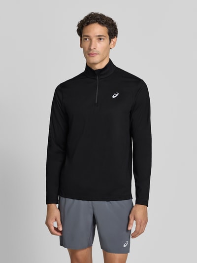 Männermodel trägt Funktionsshirt mit Logo und Reißverschluss von ASICS in Schwarz, Longsleeve aus Stretch-Material, Ganzkörperansicht von vorne.