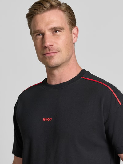 Männermodel trägt Regular Fit T-Shirt aus Baumwoll-Mix Modell 'NOAH' von HUGO in Schwarz mit roten Details, Nahaufnahme Oberkörper. Herren T-Shirt von HUGO