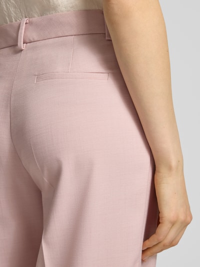Kobieta nosi Hose aus Viskose-Mix mit Bügelfalten von More & More, różowy materiał, gładka tekstura, szerokie nogawki, detal tylnej kieszeni, szerokość w rozmiarze 36: 39 cm, długość wewnętrzna nogawki w rozmiarze 36: 80 cm, widok z tyłu zbliżenie na biodro