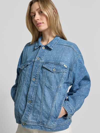 Frauenmodel trägt Regular Fit Jeansjacke mit Logo-Patch Modell 'ARCATA' von Mustang aus elastischem Baumwoll-Mix, mittleres Blau mit Umlegekragen, Brusttaschen, durchgängiger Knopfleiste und Eingrifftaschen, Struktur mit sichtbaren Nähten, Ganzkörperansicht von vorne.