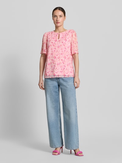 Vrouwenmodel draagt Blusenshirt mit Schlüsselloch-Ausschnitt Modell 'EMMA' van Vila in all-over look, regular fit, roze met bloemenprint, ruglengte maat 36: 60 cm, mouwlengte maat 36: 29 cm. Volledig lichaam van voren.