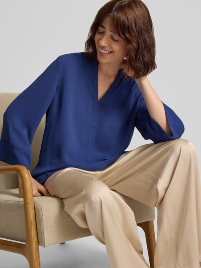 Frauenmodel trägt Regular Fit Bluse mit V-Ausschnitt und 3/4-Arm von Marc Cain in Blau, kombiniert mit beiger Hose, Nahaufnahme Oberkörper, Teilungsnähte sichtbar, Kontext: Rückenlänge bei Größe 36 71 cm, Ärmellänge 51 cm.