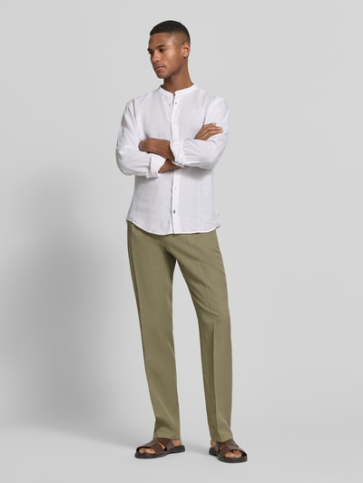 Męski model nosi spodnie materiałowe Straight Fit Stoffhose aus Lyocell-Mix Modell 'Myron' od GUESS w kolorze oliwkowym, mieszanka lyocellu, lnu i bawełny, kanty, kieszenie z tyłu, zapięcie na guzik i zamek błyskawiczny, szerokość w rozmiarze 50: 42 cm, długość wewnętrzna nogawki: 107 cm, widok całej sylwetki z przodu.