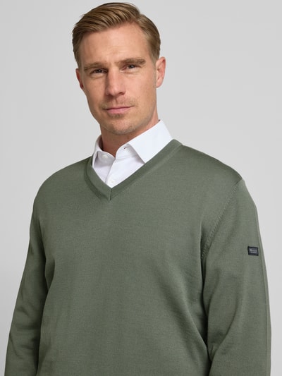 Mannelijk model draagt Strickpullover aus Schurwolle mit V-Ausschnitt van MAERZ Muenchen in olijfgroen, zuivere scheerwol, regular fit, labeldetail, ruglengte 69 cm, mouwlengte 69 cm, nahaufnahme bovenlichaam.