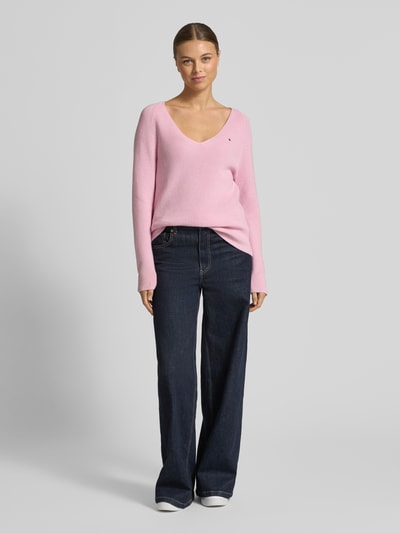Modelka nosi Regular Fit Strickpullover aus reiner Baumwolle von Tommy Hilfiger, różowy, prążkowany, dekolt V, długi rękaw, logo; widok całej sylwetki z przodu.