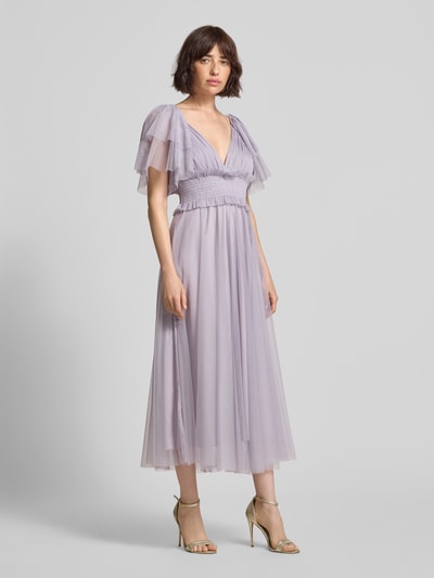 Frauenmodel trägt Midikleid mit Smok-Details und V-Ausschnitt von LACE & BEADS aus fliederfarbenem Chiffon, A-Linie, Schmetterlingsärmel, Ganzkörperansicht von vorne. Rückenlänge bei Größe S: 35 cm, Brustweite bei Größe S: 29 cm.