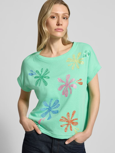 Frauenmodel trägt T-Shirt aus Baumwoll-Leinen-Mix mit Stitchings von Milano Italy, grün mit bunten Blumenmustern, Rundhalsausschnitt, Ganzkörperansicht von vorne.