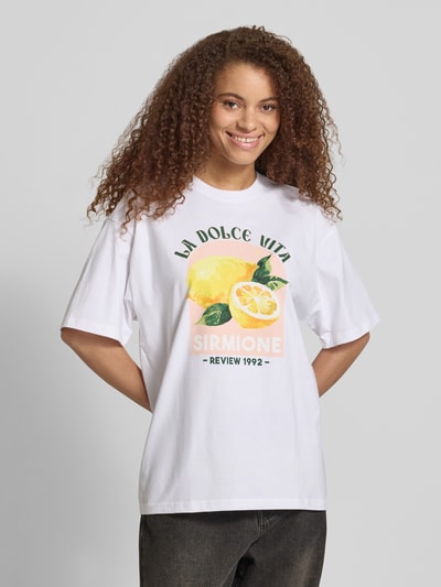 Frauenmodel trägt T-Shirt mit rückseitigem Motiv-Print von REVIEW, Damen T-Shirt aus reiner Baumwolle, oversized, Weiß mit buntem Print, Rundhalsausschnitt, Rückenlänge bei Größe S 68 cm, Ganzkörperansicht von vorne.
