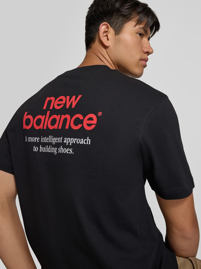 Männermodel trägt Regular Fit T-Shirt aus reiner Baumwolle Modell 'INTELLIGENT' von New Balance, schwarzer Stoff mit rückseitigem Print, Kontext: Herren T-Shirt, Label-Detail, Rückenlänge Größe M 72 cm, Ganzkörperansicht Rückansicht.