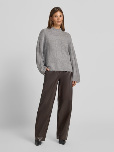 Frauenmodel trägt Oversized Wollpullover mit Kaschmir-Anteil von Emporio Armani in Grau mit Stehkragen, Strukturmuster und gerippten Abschlüssen, Schurwoll-Kaschmir-Mix, kombiniert mit weiter brauner Hose, Ganzkörperansicht von vorne.