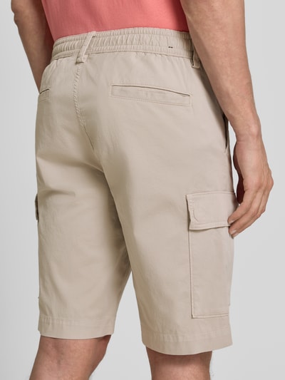 Männermodel trägt Relaxed Fit Cargoshorts aus Baumwoll-Mix Modell 'SISLA' von BOSS Orange, Optik: Unifarben, Passform: Relaxed-Fit, Label-Patch, seitliche Eingrifftaschen, Gesäßtaschen, Cargotaschen, Farbe Beige, Material Baumwoll-Mix, Ganzkörperansicht Rückansicht.