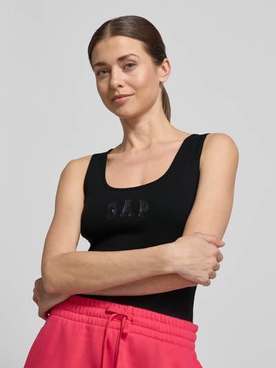 Frauenmodel trägt Slim Fit Top mit Logo-Print von GAP in Schwarz aus elastischem Baumwoll-Mix, mit Rundhalsausschnitt, Nahaufnahme Oberkörper.