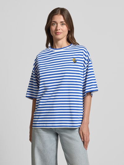 Kobiece modelka nosi damski t-shirt Oversized T-Shirt aus reiner Baumwolle Modell 'JARINERO STRIPED' od Essentiel Antwerp, efekt: wzór w paski na całej powierzchni, krój oversized, wyhaftowany motyw, okrągły dekolt, rękaw o dł. 1/2, wykończenie: dżersej, materiał: czysta bawełna, jasnoniebieskie i białe paski, widok na cały przód.